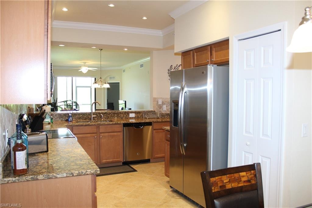 Kitchen with decorative light fixtures, brown cabinetry, ornamental molding, appliances with stainless steel finishes, and dark stone counters