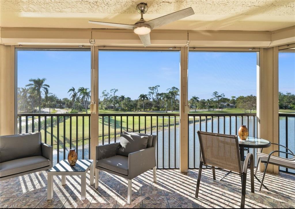 Enclosed balcony with tiled flooring, ceiling fan, and expansive water and golf course scenery