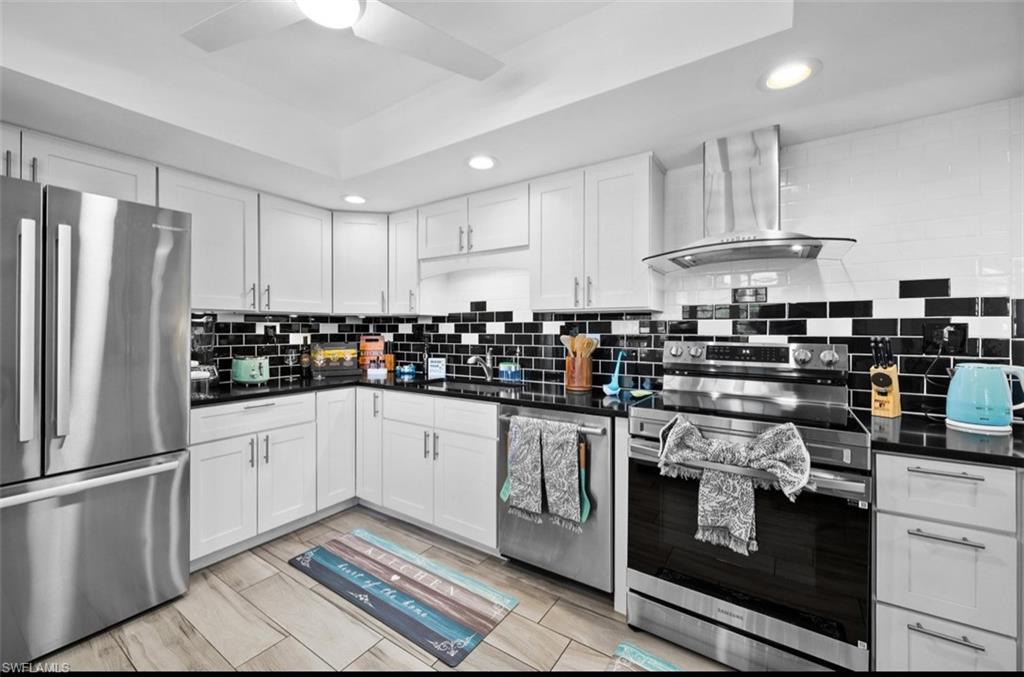 Kitchen featuring stainless steel appliances, black countertops, white cabinetry, a black and white tile backsplash, and wood-finish flooring