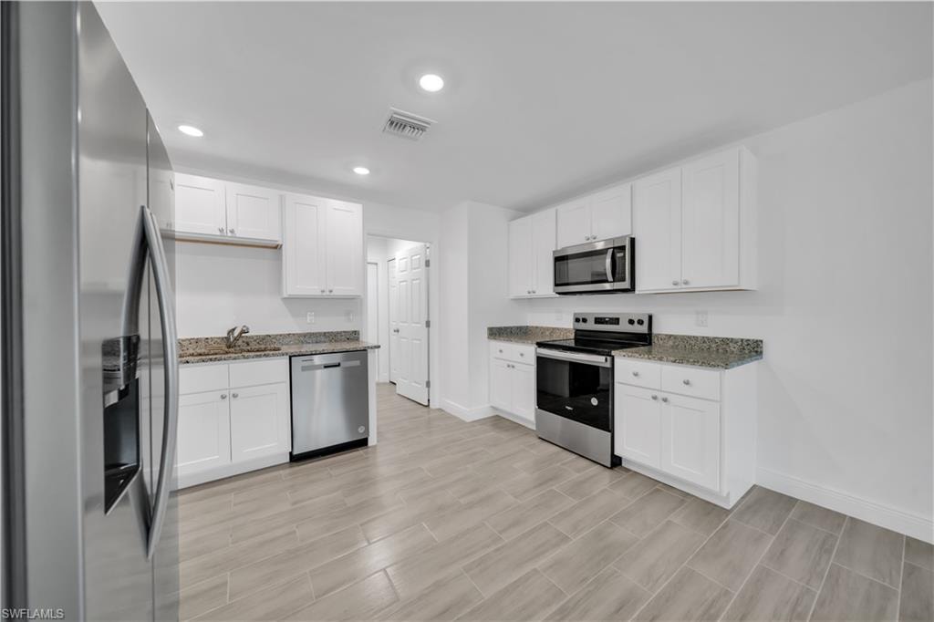 Kitchen featuring white cabinetry, stone-finish countertops, stainless steel appliances, and tiled flooring