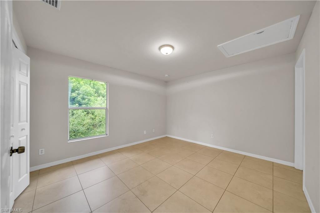 Spacious room featuring neutral wall tones, large-format tile flooring, a single window, and a flush-mount ceiling light