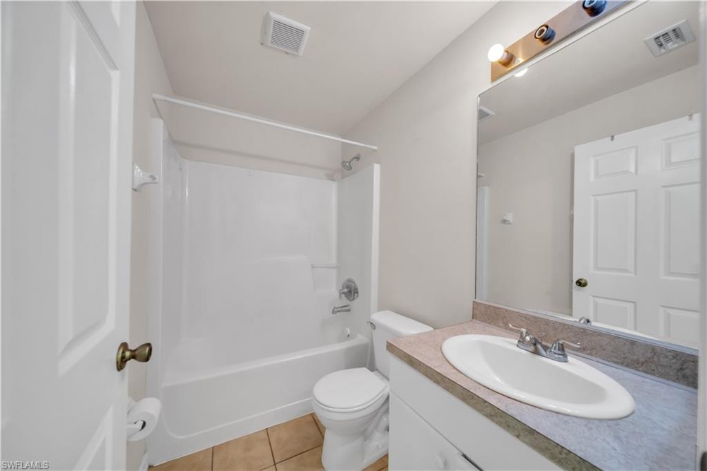 Bathroom featuring a white shower-over-tub combination, a vanity with an integrated sink, a rectangular mirror, and tile flooring