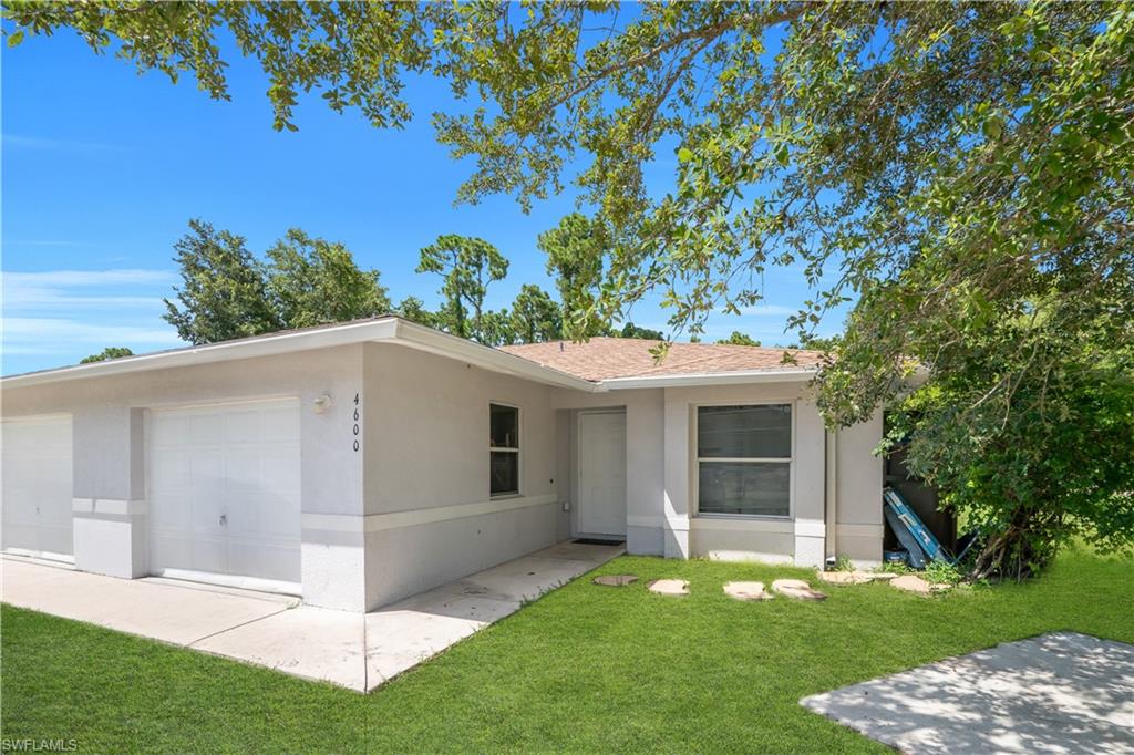 Modern single-story residence featuring a clean stucco exterior with a covered carport, expansive manicured lawn, mature shade trees, and defined concrete walkways throughout the property