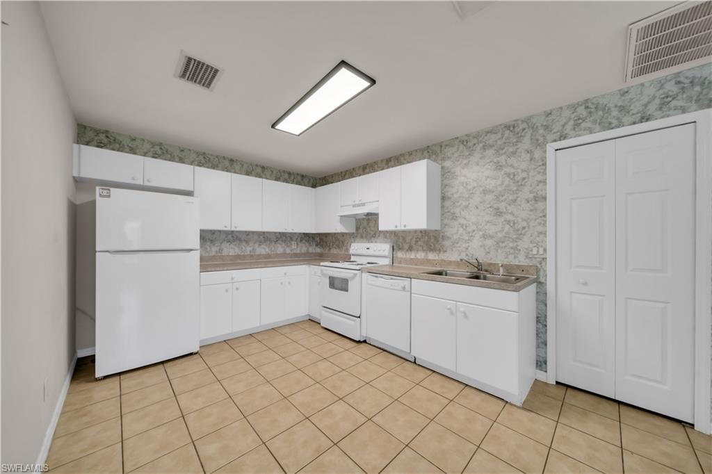 Kitchen featuring L-shaped cabinetry, neutral tile flooring, laminate countertops, and a double basin sink