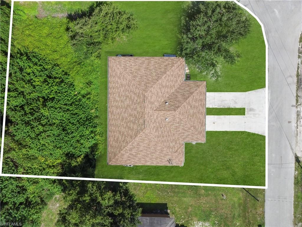 Expansive property featuring a shingled roof, a concrete driveway, and a spacious green lawn