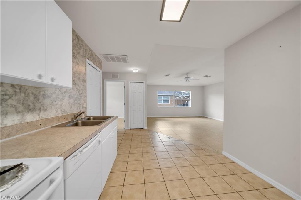 Bright, open-concept kitchen and living area featuring white cabinetry, tile countertops, ceramic tile flooring, and abundant natural light from multiple windows