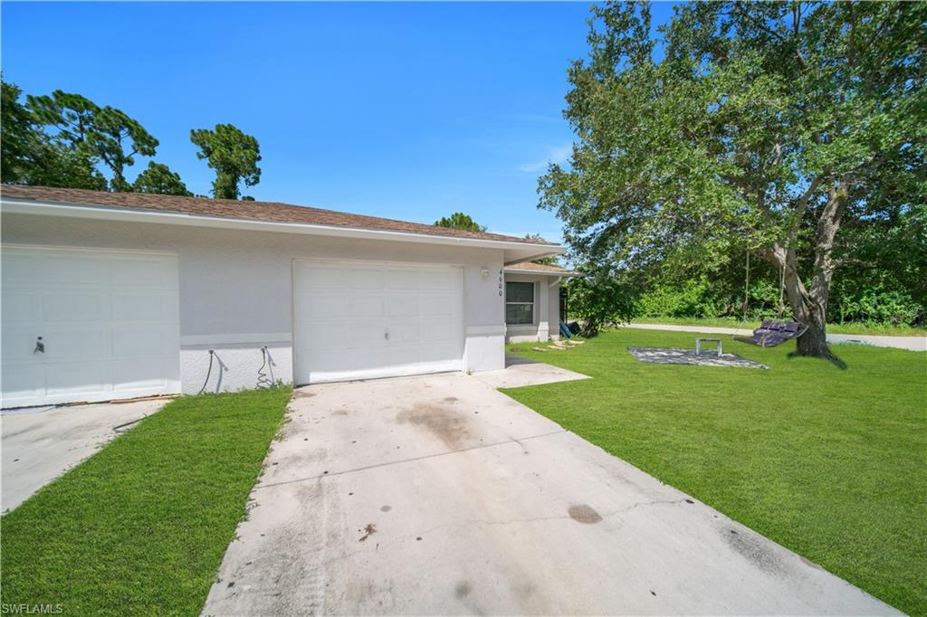 Exterior featuring a two-car garage, concrete driveway, and expansive lawn with mature trees