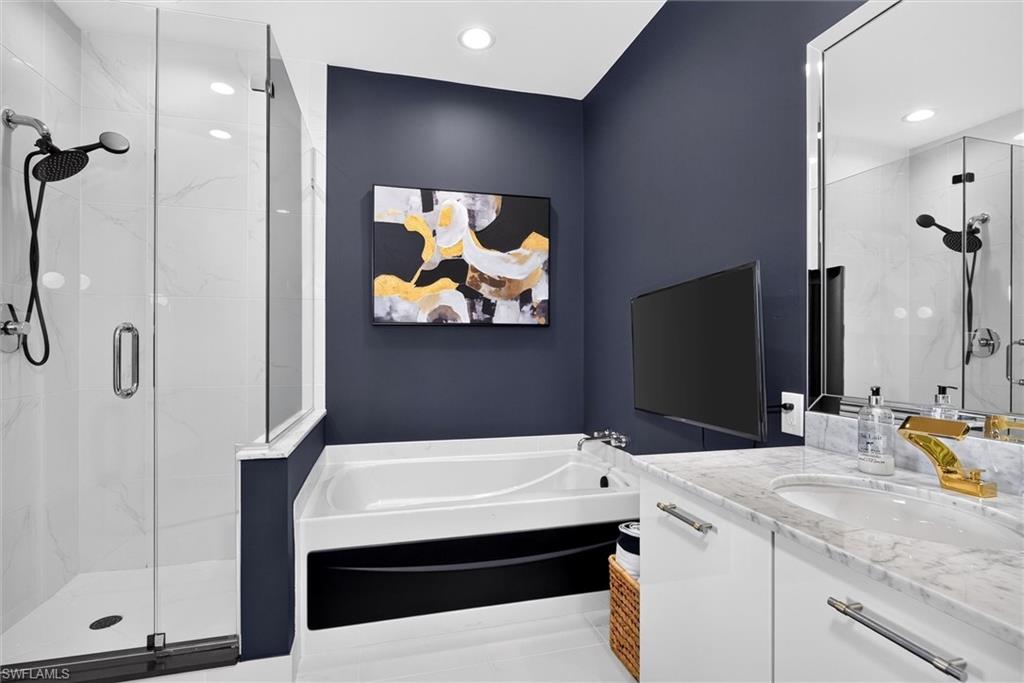 Glass-enclosed shower with a handheld fixture, white soaking tub, single vanity with a stone countertop, and a large wall-mounted mirror