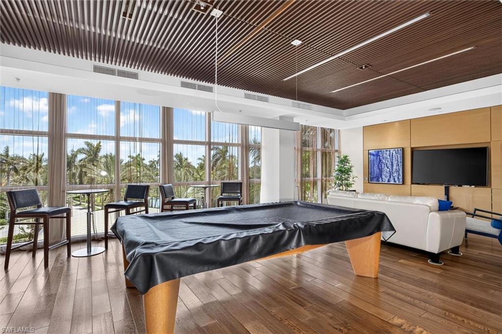 Expansive room featuring wood-finish flooring, a wood slat ceiling with integrated lighting, a wall of floor-to-ceiling windows, and a built-in media wall