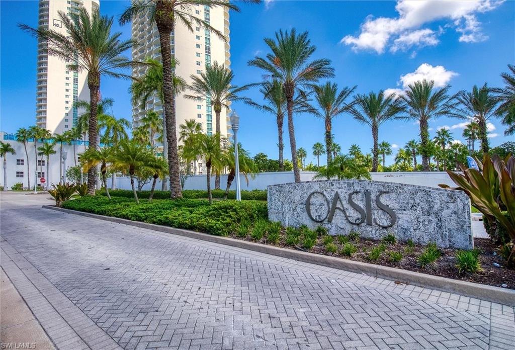Paver driveway entry with integrated landscaping, mature palm trees, and a stone monument sign