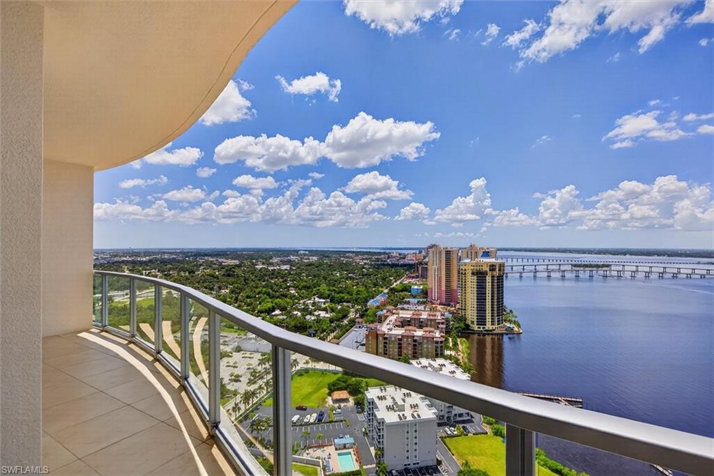 Curved balcony with tile flooring and a glass railing, featuring expansive water and cityscape scenery