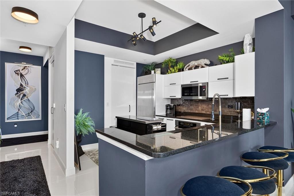 Open-concept kitchen with a breakfast bar, dark granite countertops, white cabinetry, and stainless steel appliances