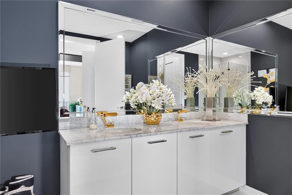 Dual vanity with white cabinetry, gold-tone fixtures, and a light-toned countertop, framed by multiple wall mirrors