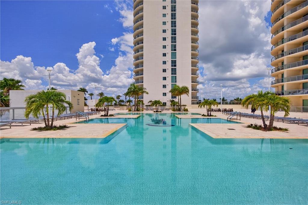 Resort-style pool with integrated sun shelves, surrounded by palm trees and a light-toned paved deck