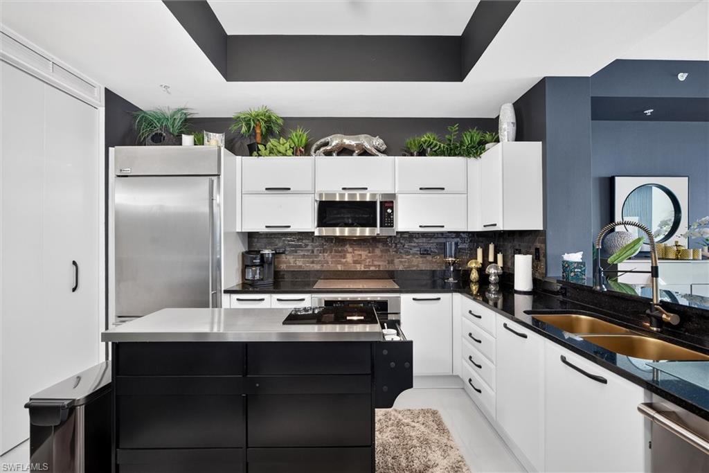 Kitchen featuring white cabinetry with black hardware, black countertops, stainless steel appliances, and a central island with a stainless steel top