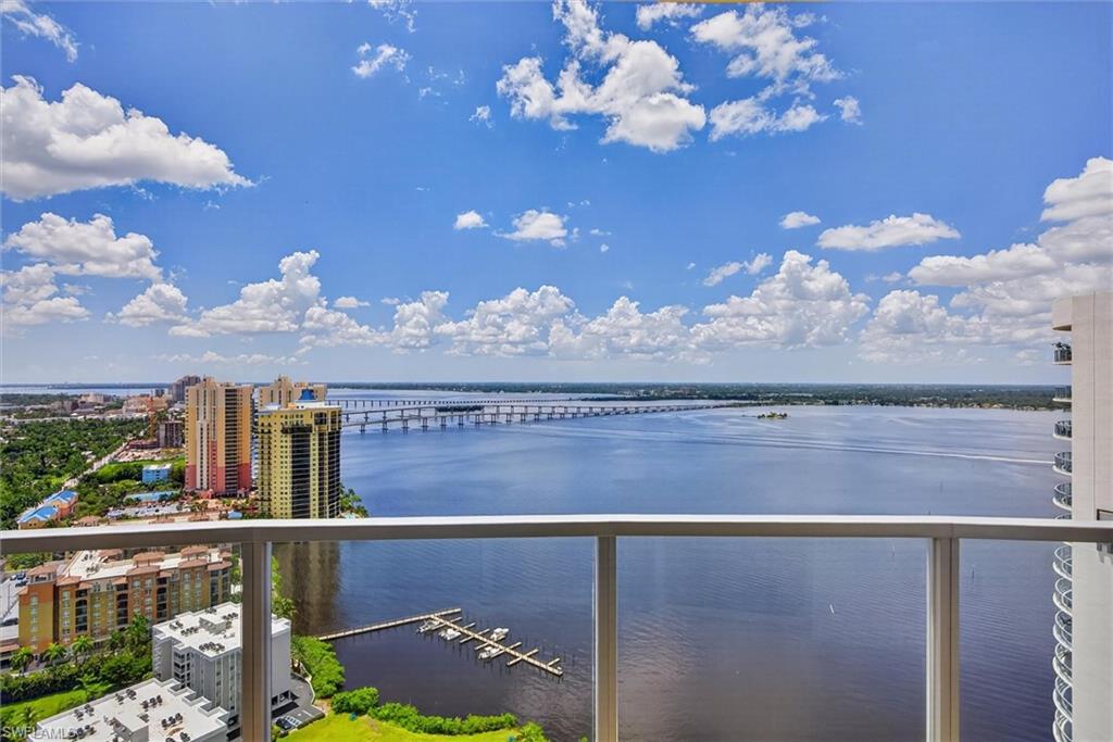 Balcony with glass panel railing and aluminum top rail, offering expansive water scenery, a distant bridge, and city buildings