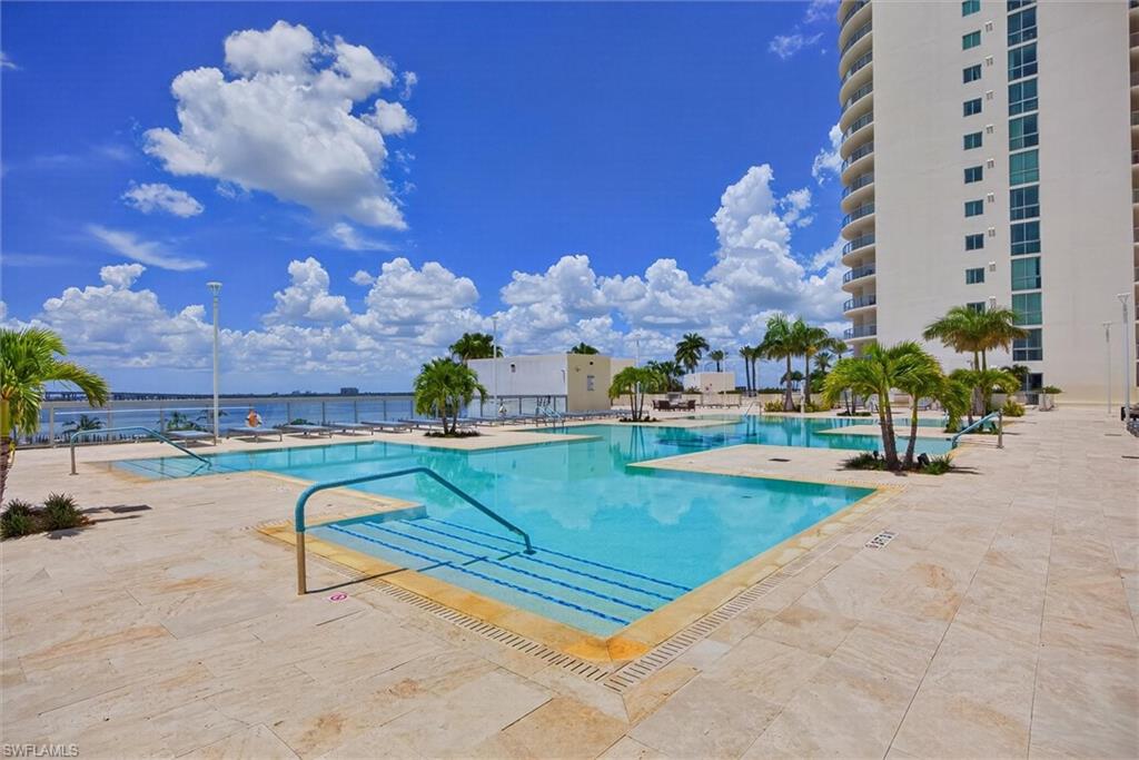 Expansive resort-style pool deck with multiple swimming areas, surrounded by mature palm trees and light-toned tile paving
