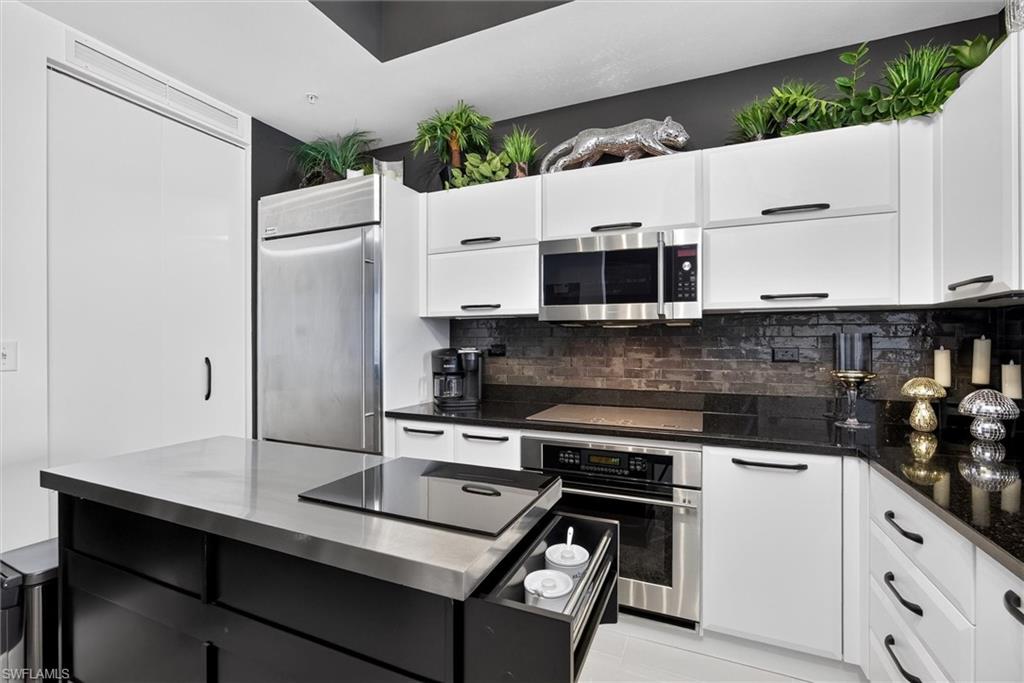 Kitchen featuring white cabinetry, stainless steel appliances, dark stone countertops, and a dark stone tile backsplash
