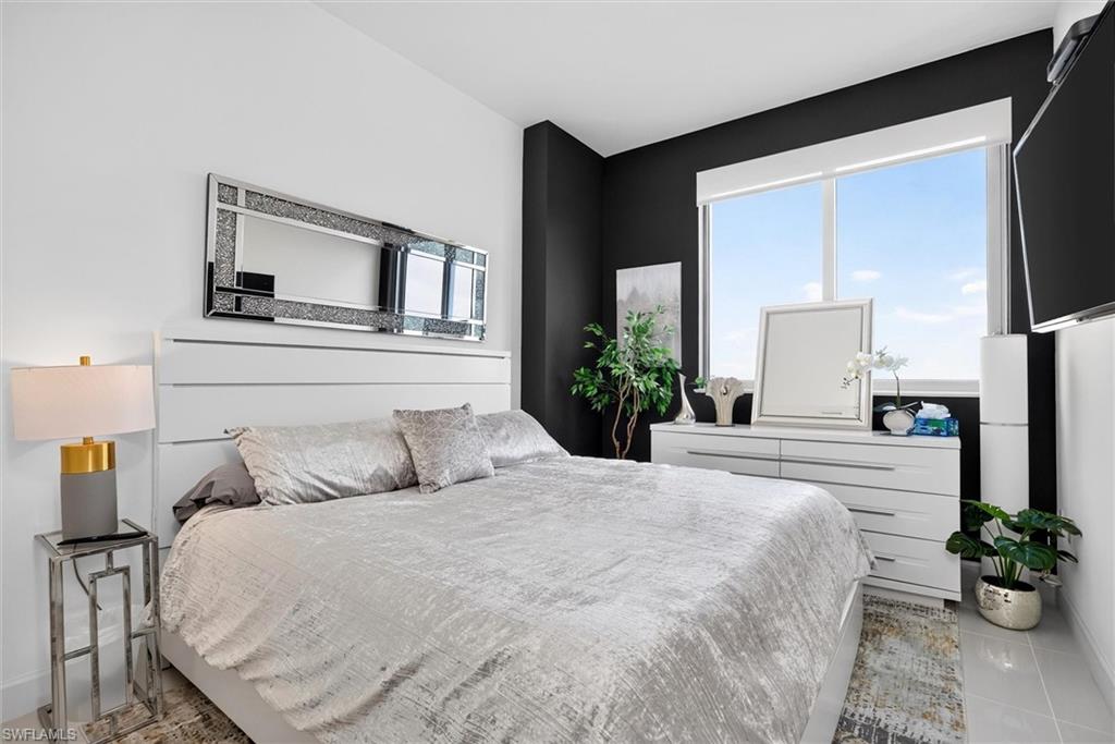 Expansive window with roller shade, sleek white dresser with six drawers, and a built-in wall-mounted television