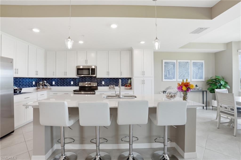 Kitchen featuring white cabinetry, stainless steel appliances, a spacious island with counter seating, blue subway tile backsplash, and recessed lighting