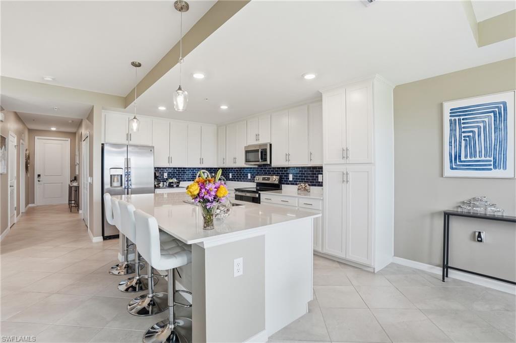 Kitchen featuring a large central island, stainless steel appliances, extensive white cabinetry, a dark blue subway tile backsplash, and recessed lighting