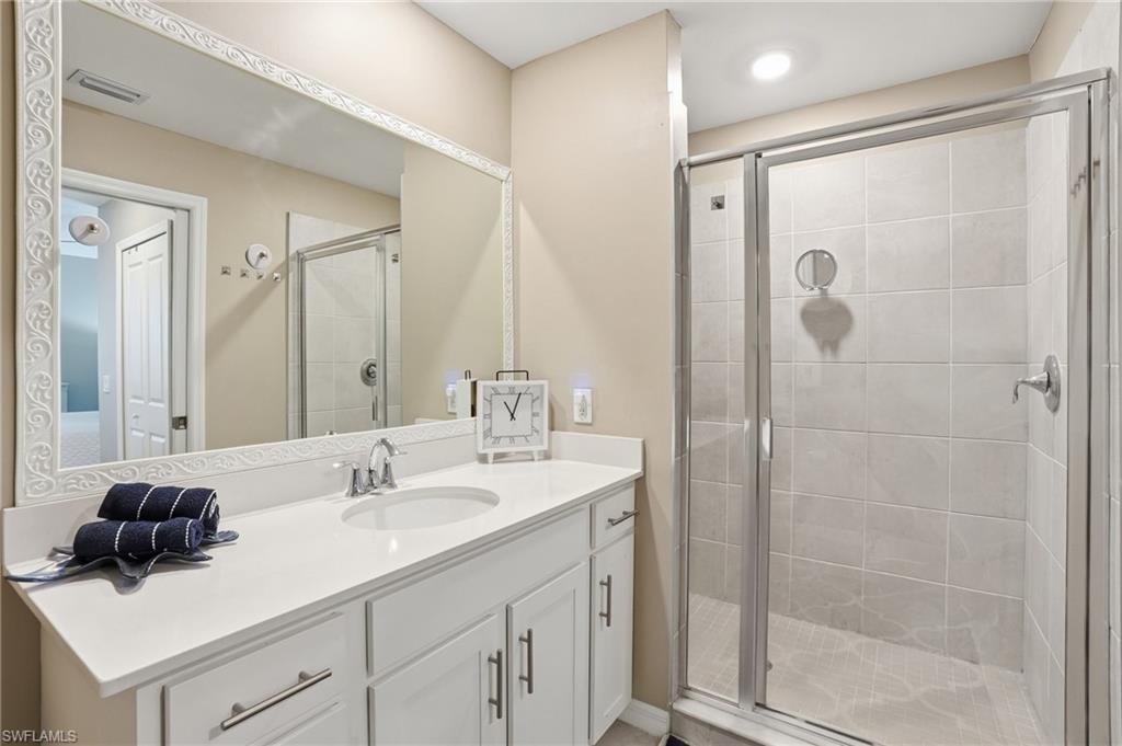 Vanity with a white countertop and undermount sink, framed mirror, glass-enclosed shower, and tiled shower walls