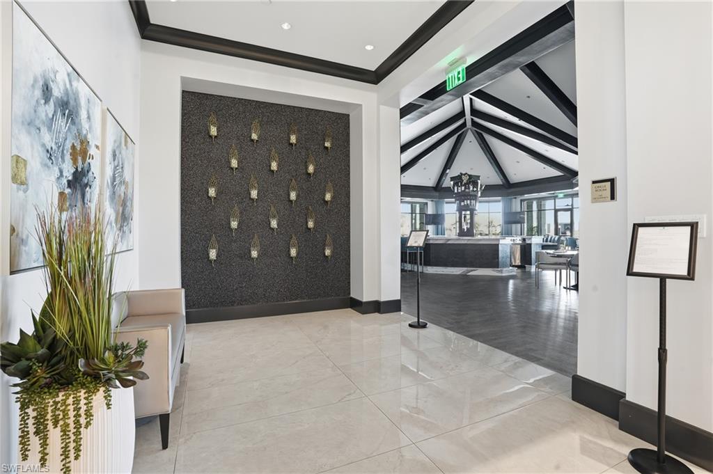 Tiled entryway featuring a textured accent wall with sconces and dark trim, leading to a vaulted-ceiling space with exposed beams