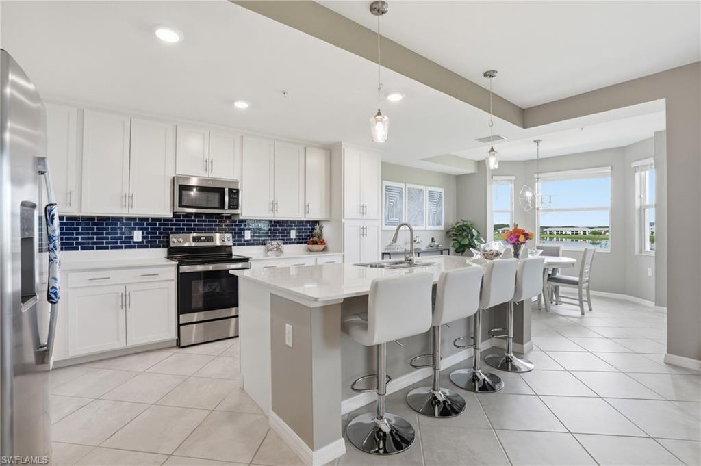Kitchen featuring white cabinetry, stainless steel appliances, a blue subway tile backsplash, an island with seating, and tiled flooring