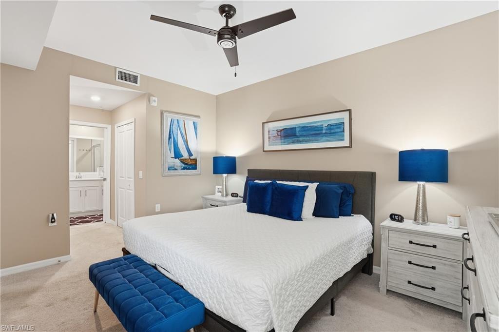 Carpeted bedroom with a dark-bladed ceiling fan, neutral wall tones, and an attached ensuite featuring a vanity with white cabinetry