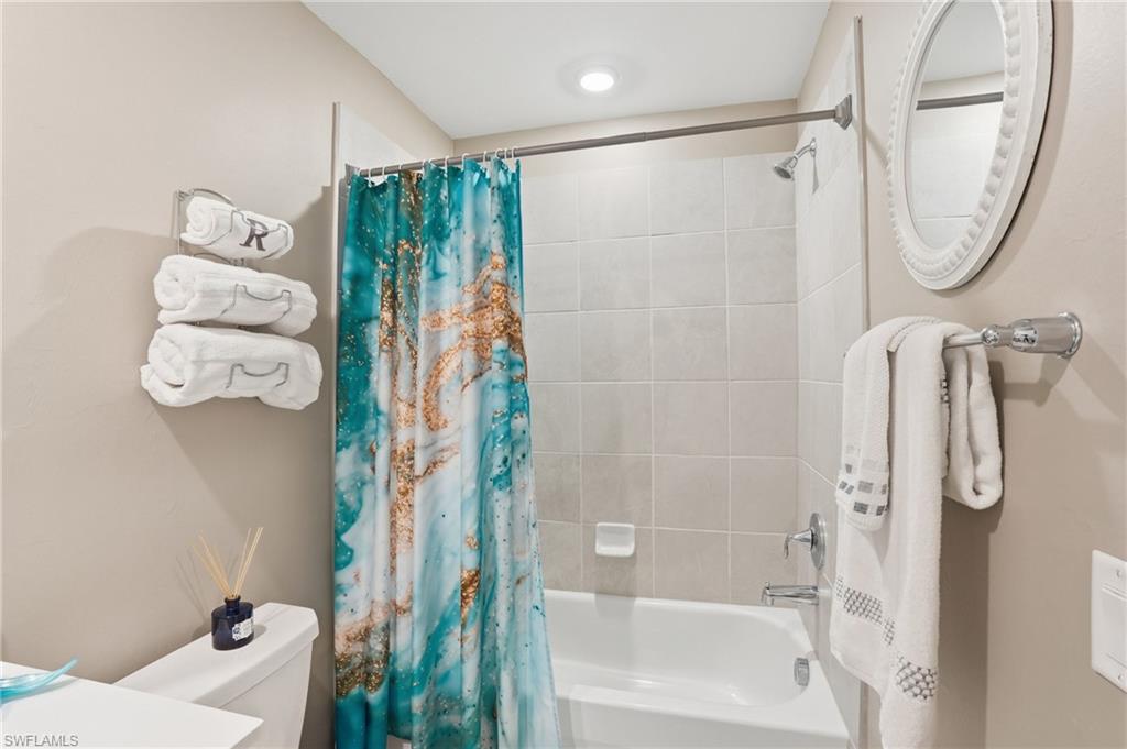 Recessed lighting illuminates the bath/shower combination with light-toned wall tiling