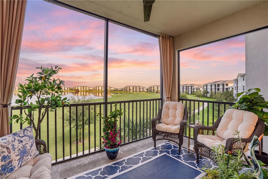 Screened balcony featuring a ceiling fan, a railing, and a water body with surrounding buildings