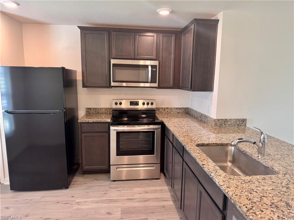 Kitchen featuring stainless steel appliances, dark brown cabinetry, light stone countertops, and light wood-style floors