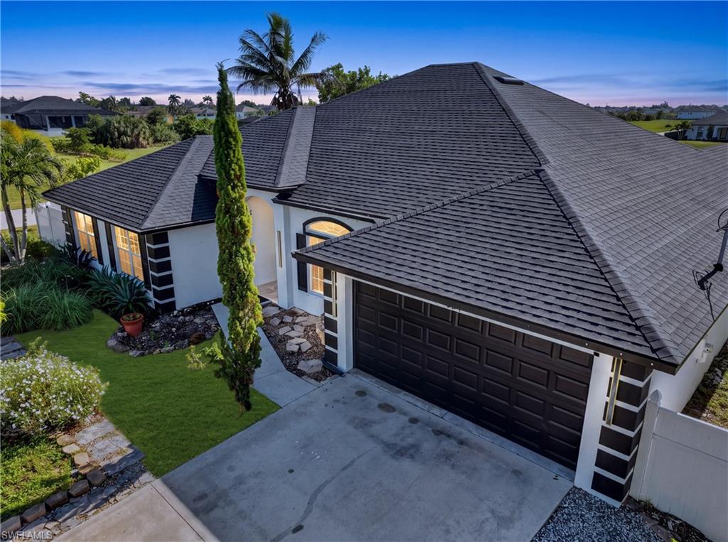 Pitched shingle roof, arched entryway, attached garage, concrete driveway, and a manicured lawn