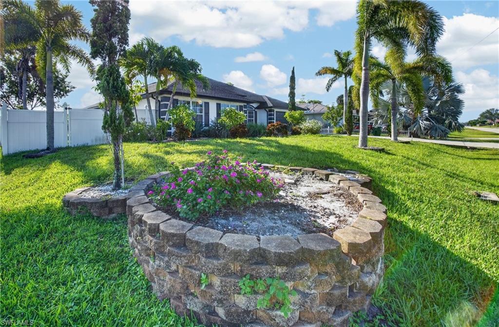 Landscaped front yard featuring a block retaining wall, mature palm trees, and a white privacy fence
