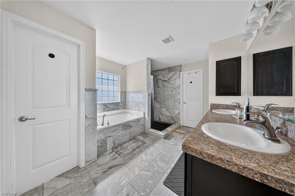 Dual vanity with integrated sinks, a built-in soaking tub, a separate shower with tiled walls, and tiled flooring