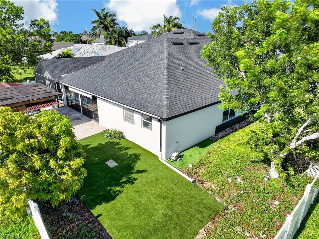 Pitched roof with multiple skylights, screened patio area, white stucco exterior, and a manicured lawn