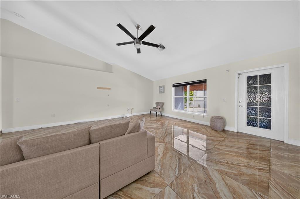 Vaulted ceilings, large format tile flooring, modern ceiling fan, large window with blinds, and a decorative glass paneled door