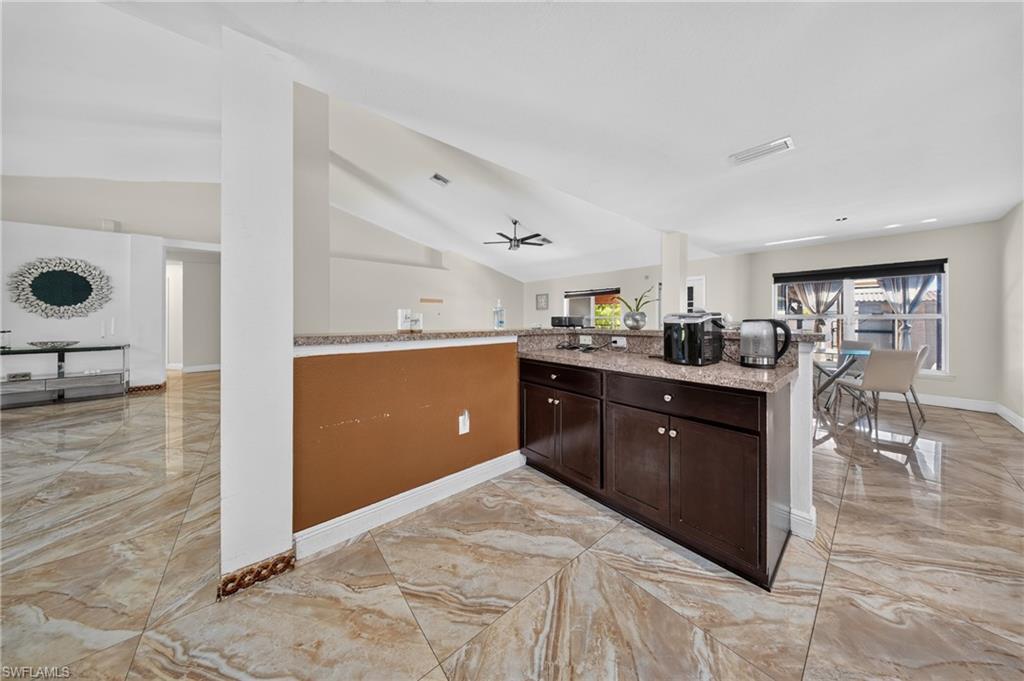 Open-concept layout with vaulted ceilings, large windows, dark wood-finish cabinetry, and light-toned tile flooring