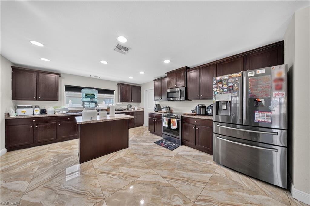 Kitchen featuring dark wood cabinetry, a central island, stainless steel appliances, and large format floor tiling
