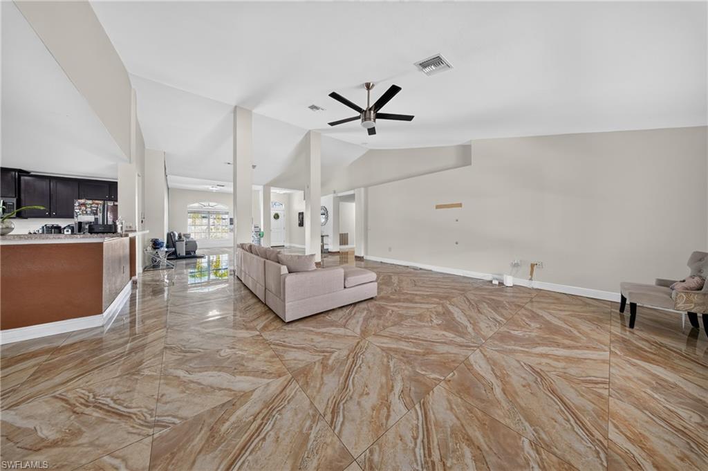 Vaulted ceilings, a dark wood-finish ceiling fan, and large format polished tile flooring