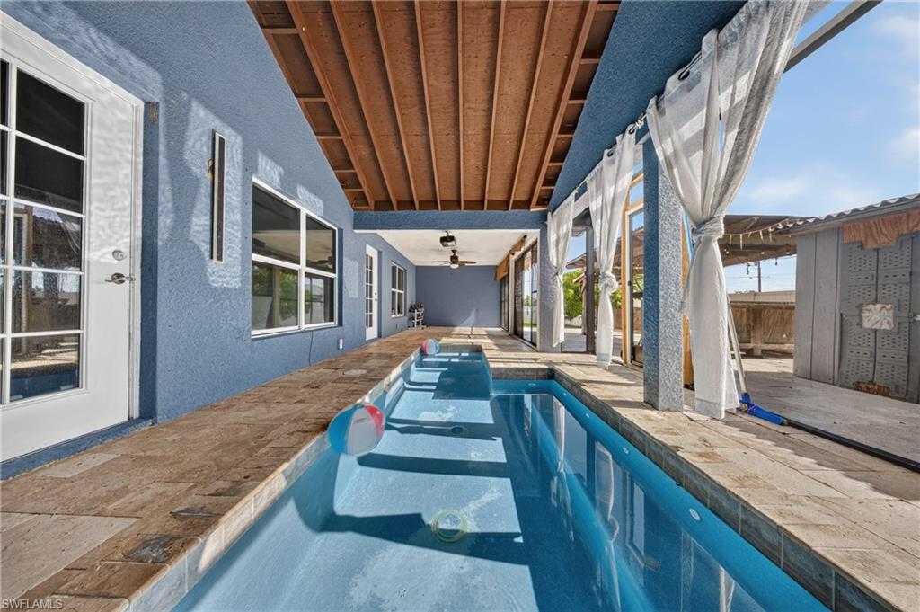 Covered patio featuring an elongated swimming pool with a stone coping, exposed wood beam ceiling, and multiple glass-paned doors