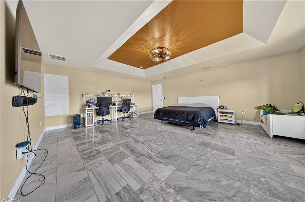 Tray ceiling with accent paint and chandelier, light-toned walls, and large format tile flooring