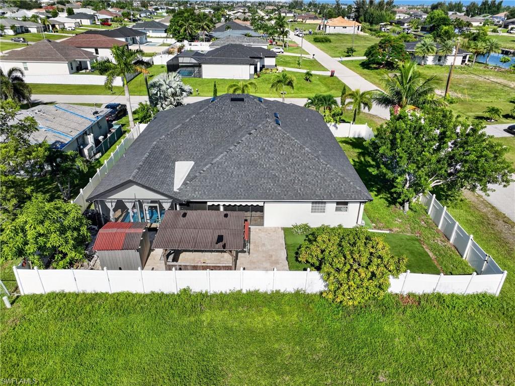 White privacy fencing, stone patio, outdoor covered structure, and mature landscaping