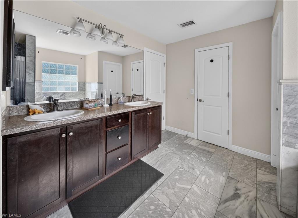 Dual vanity with dark wood-finish cabinetry, light-colored countertops, undermount sinks, and an expansive wall-mounted mirror