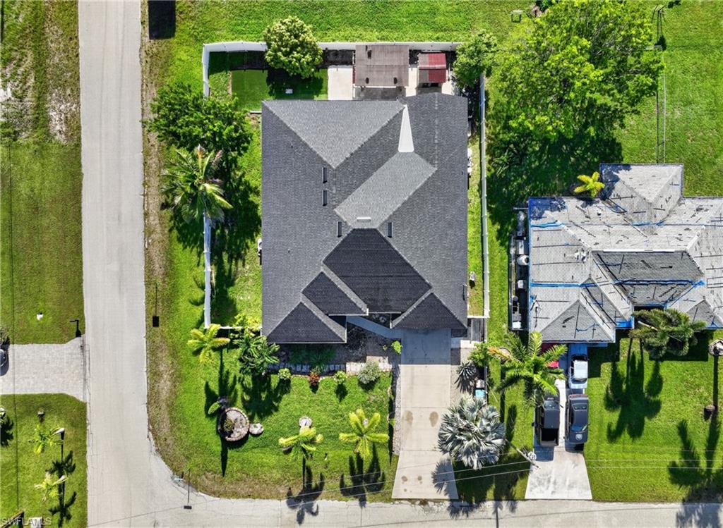 Property with a dark shingle roof, green lawn, and mature palm trees