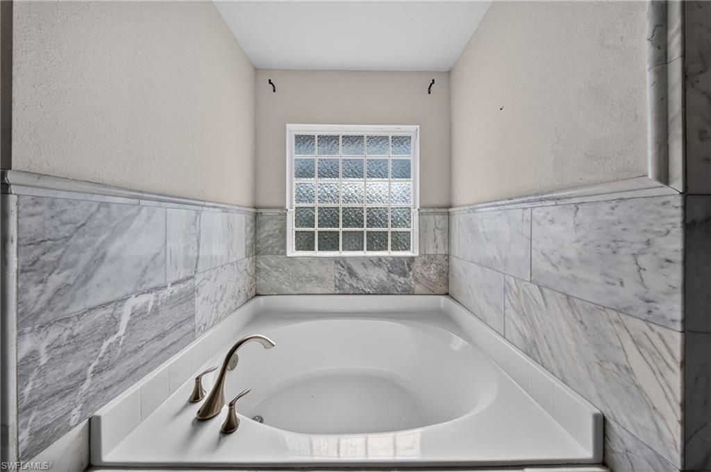 Soaking tub with brushed nickel fixtures, surrounded by large format wall tile, a textured privacy window, and a built-in tub deck