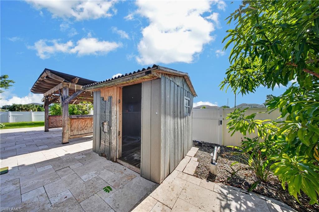 Hardscaped patio area with light-toned pavers, featuring a detached shed and a covered outdoor bar structure
