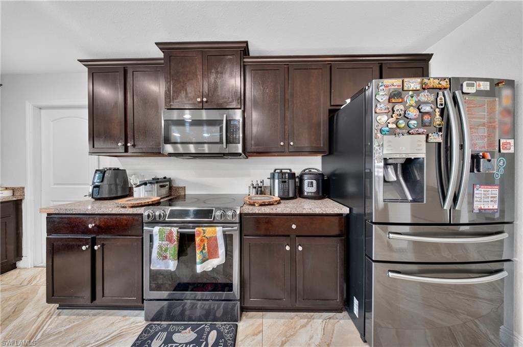 Kitchen featuring dark wood cabinetry, light-toned countertops, stainless steel appliances, and a tile floor