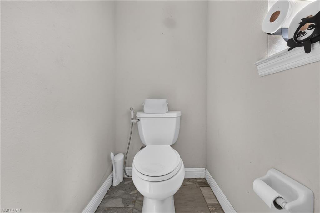 White toilet with an attached bidet sprayer, tile flooring, and white trim