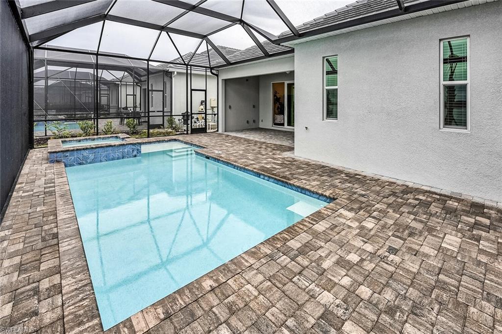 View of pool featuring glass enclosure, a pool with connected hot tub, and a patio area